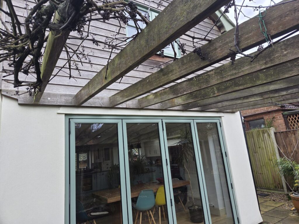 Timber pergola above bi-fold doors with mature climbing vines