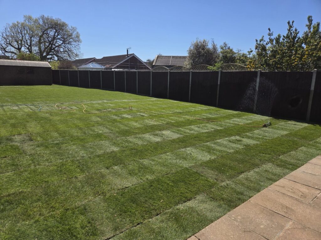 Newly finished garden with levelled turf surrounded by patio and wooden fencing